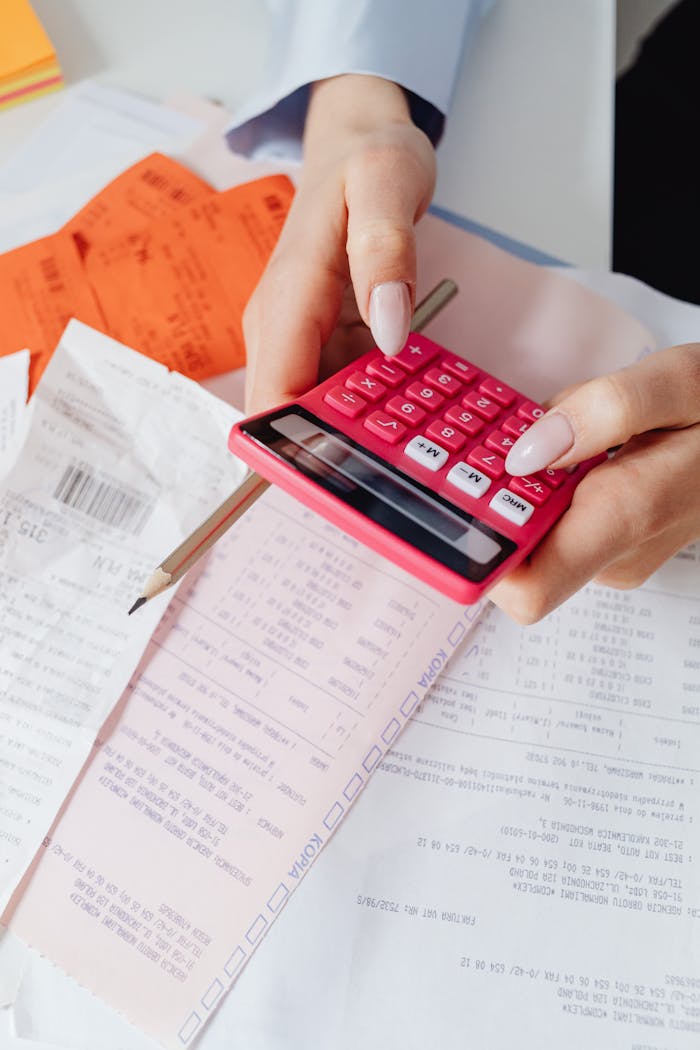 Hands using a red calculator surrounded by financial documents and receipts, symbolizing financial management.